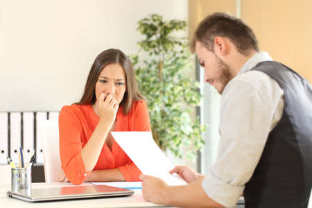 Nervous woman looking at manager reading her resume during a job interview at officeの写真素材