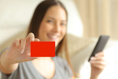 On line buyer holding a smart phone is showing a blank credit card and looking at cameraの写真素材