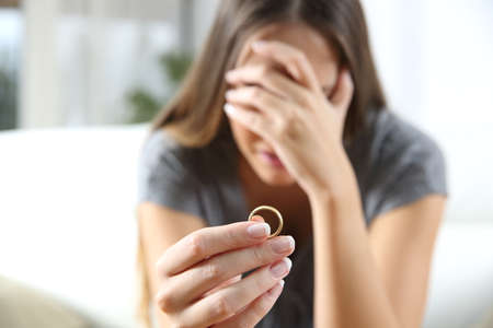 Closeup of a single sad wife after divorce lamenting holding the wedding ring in a house interiorの写真素材
