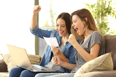 Excited roommates reading a bank notification sitting on a sofa in the living room at homeの写真素材