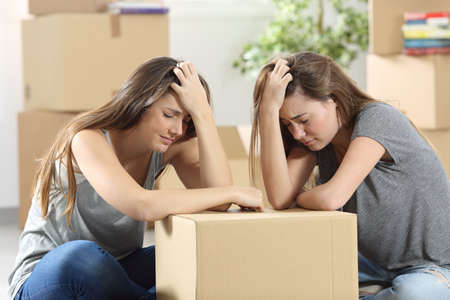 Sad roommates moving house together after eviction sitting on the floor at homeの写真素材