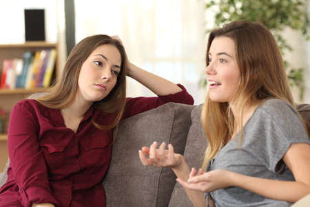 Bored girl listening to her friend having a conversation sitting on a couch in the living room at homeの写真素材
