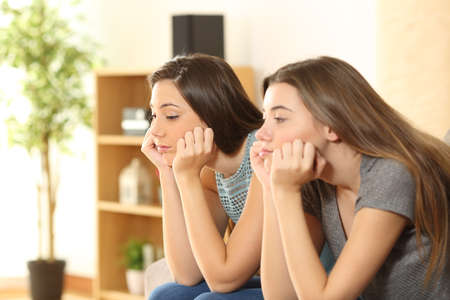 Bored roommates or friends sitting on a sofa in the living room at homeの写真素材