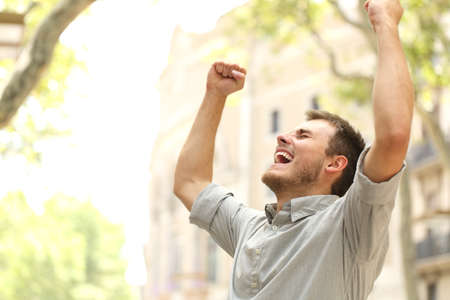 Portrait of an excited man raising arms in the street with buildings in the background