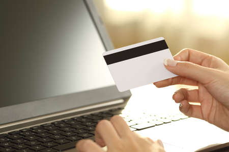 Girl hands holding credit card and buying on line sitting on a couch in the living room at home with a warm light in the backgroundの写真素材