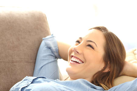 Portrait of a single happy woman relaxing and laughing after work lying on a sofa in the living room at homeの写真素材