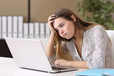 Frustrated intern trying to work on line with a laptop in a difficult assignment in a desktop with an office backgroundの写真素材
