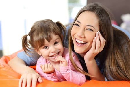 Front view portrait of a happy mother and daughter looking to camera in the living room at home