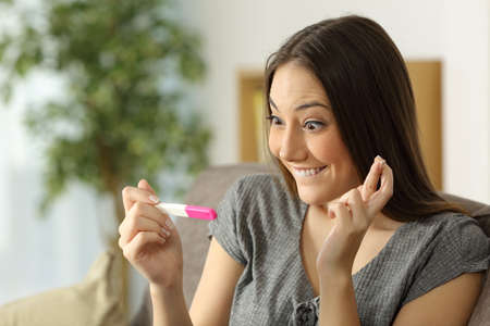 Hopeful woman checking a pregnancy test sitting on a couch in the living room at homeの写真素材