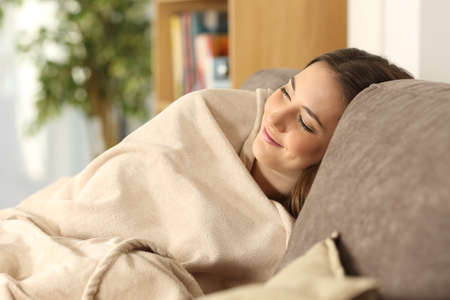 Relaxed girl sleeping covered with a warmly blanket sitting on a comfortable couch in the living room at homeの写真素材