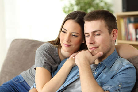 Pensive couple thinking sitting on a sofa in the living room at homeの写真素材