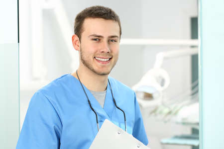 Doctor male posing and looking at you in an dentist office with medical equipment in the backgroundの写真素材