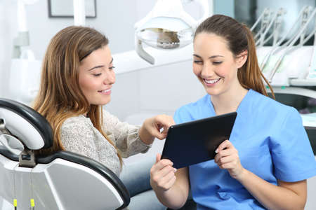 Dentist and patient choosing treatment in a consultation with medical equipment in the backgroundの写真素材