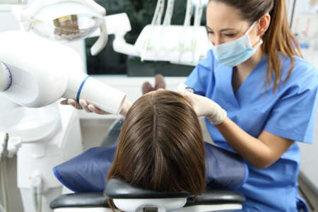 Dentist taking x-ray of patient teeth in a clinic box with medical equipment in the backgroundの写真素材