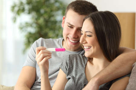 Happy couple checking pregnancy test sitting on a couch in the living room at homeの写真素材