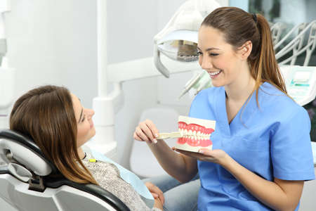 Dentist explaining how to brush teeth correctly to a patient after treatments sitting on a chair in a clinic box with medical equipment in the backgroundの写真素材