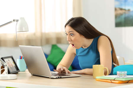 Single amazed student searching on line content in a laptop sitting in a desk in her room in a house interiorの写真素材