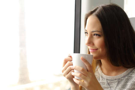 Happy pensive train or bus passenger looking through window holding a cup of coffeeの写真素材