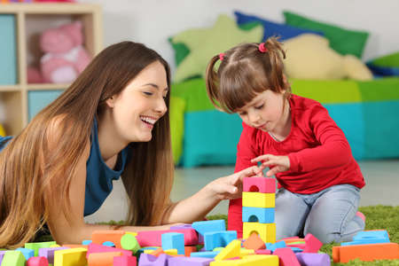 Mother and daughter playing together with colorful construction toys on a carpet on the floor af a bedroom at homeの写真素材