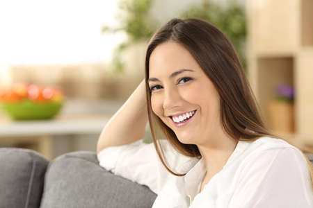 Single beauty woman with perfect white teeth smiling and looking at you sitting on a sofa in the living room at homeの写真素材
