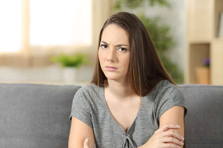 Angry woman looking at you sitting on a sofa in the living room at homeの写真素材