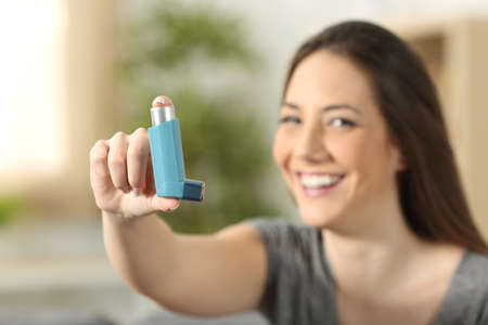 Girl showing an asthma inhaler sitting on a couch in the living room at homeの写真素材