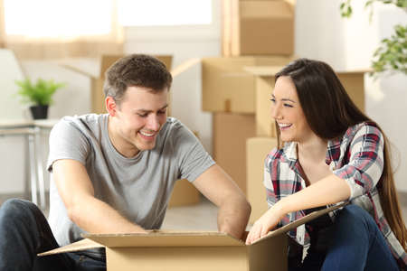 Couple moving home packing belongings in a cardboard box sitting on the floor of the living roomの写真素材