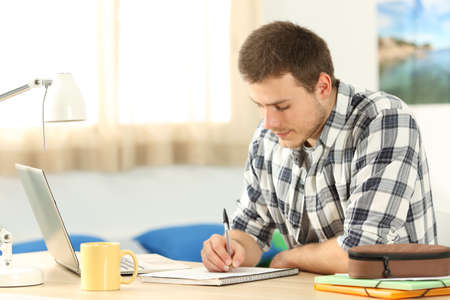 Portrait of a student writing in a notebook doing homework in a desk in his roomの写真素材