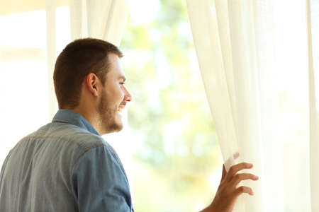 Single pensive man looking outdoors through a window at home or hotelの写真素材