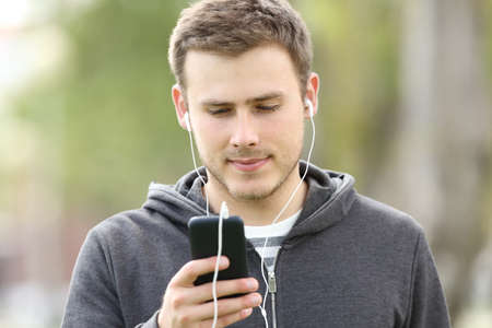 Front view portrait of a teen listening music on line with earbuds and watching media content on a smart phoneの写真素材