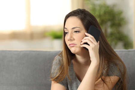 Casual woman bored during a phone call sitting on a couch in the living room in a house interior with a homey backgroundの写真素材