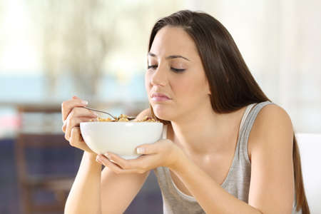 Disgusted woman eating cereals with bad taste at homeの写真素材