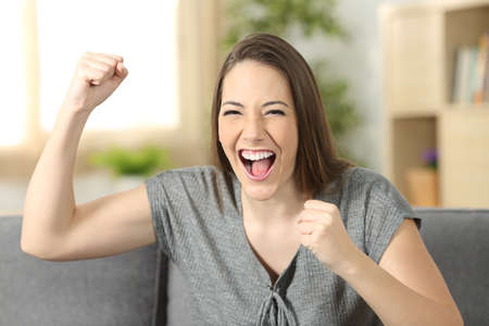 Excited woman looking at you sitting on a sofa in the living room at homeの写真素材