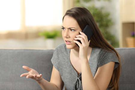 Angry woman arguing during a phone call sitting on a couch in the living room at homeの写真素材