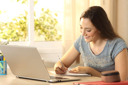 Portrait of a student studying taking notes sitting in a table at homeの写真素材