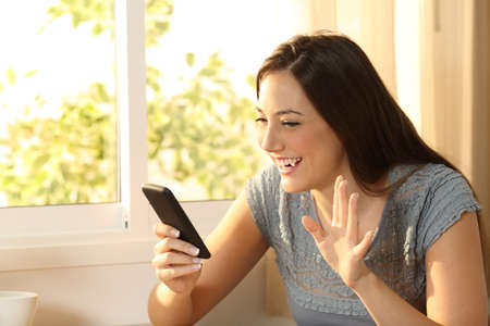 Happy girl waving during an on line phone video call at homeの写真素材
