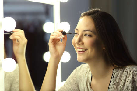 Single happy woman making up eyelashes in front of a mirror at homeの写真素材