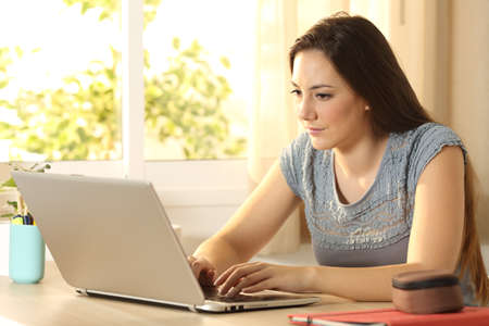 Casual serious student searching on line typing in a laptop on a desk at home with a warm light in the backgroundの写真素材