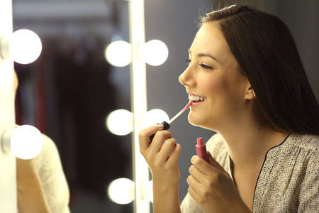 Single girl painting lips with a glossy lipstick in front of a make up mirror at homeの写真素材