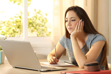 Serious student learning on line watching content in a laptop sitting in a table in her room at homeの写真素材