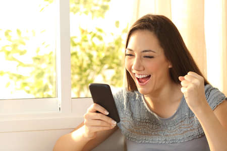 Single excited woman watching content on a smart phone at homeの写真素材