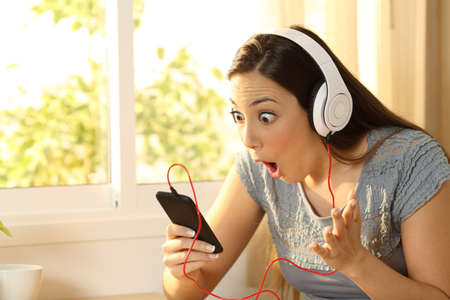 Amazed woman listening music finding offers on line in a smart phone in her roomの写真素材