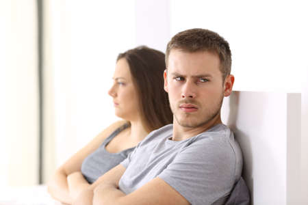 Angry couple after argument looking at another side sitting on the bed at homeの写真素材