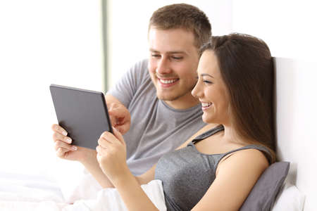 Couple watching media content together on line in a tablet on the bed of an apartmentの写真素材
