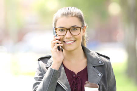 Front view of a fashion satisfied girl talking on the phone and looking at you in the streetの写真素材