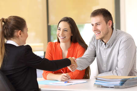 Couple of happy customers handshaking with worker after a deal at officeの写真素材