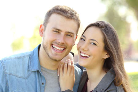 Front view of a couple posing outdoors with perfect smile and white teeth and looking at you in a park with a green background