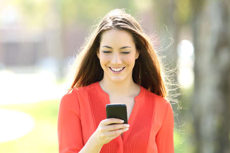 Front view portrait of a single woman walking towards camera using a smart phone on line in the streetの写真素材