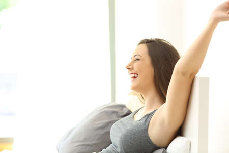 Side view of a single excited woman raising arms and waking up sitting on a bed of an hotel room or...