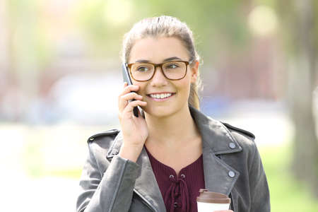 Front view of a fashion girl walking towards camera and calling on mobile phoneの写真素材